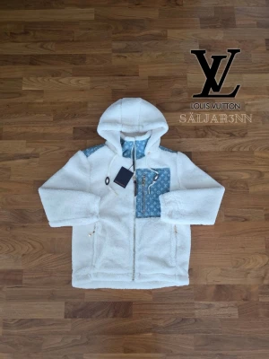 Vit teddyjacka - Säljer en fluffig vit teddyjacka med huva och dragkedja. Jackan har blå detaljer med monogram på bröstficka, axel och insida. Två sidofickor med dragkedja och en unik design som sticker ut. Perfekt för dig som vill ha något exklusivt och trendigt.