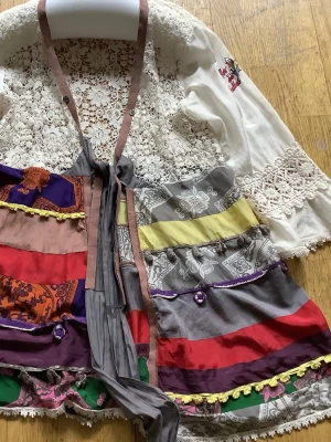 Färgglad bohemisk klänning med spets - Unik blus från Odd Molly( puppa silk wrap i bohemisk stil med virkade spetsdetaljer upptill och på ärmarna. Klänningen har långa ärmar, knytband i midjan och färgglada patchwork-paneler i rött, lila, grått, gult, grönt och orange. Dekorerad med volanger och små pärlor för extra detalj.En klassisk modell från tiden 07-09.