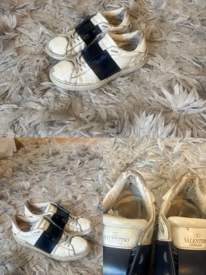 Valentino Garavani Open Sneaker - Snygga vita Valentino Garavani Open sneakers i kalvskinn med en bred marinblå läderdetalj över mitten. Klassisk låg modell med rund tå, platt sula och diskret logga på plösen. Perfekta för dig som vill ha en clean men lyxig look.