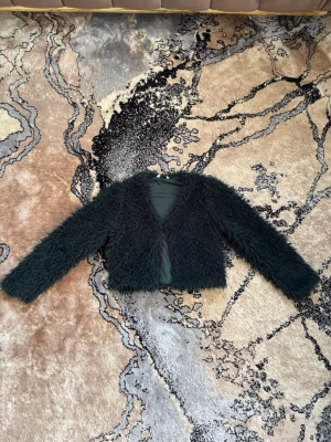 Mörk grön fluffig pälsjacka - Säljer en mörk grön, kort pälsjacka med lång ärm och öppen framtill. Jackan har en riktigt fluffig och mjuk look som ger en trendig vibe. Perfekt för dig som vill sticka ut och hålla värmen under kalla dagar. Passar perfekt för bröllop, fester och andra eleganta ställen. Materialet är fuskpäls. Anledningen till att jag säljer den är på grund av att det inte passar min ålder längre. 