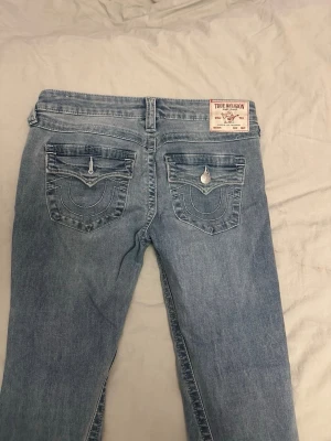 Blå jeans från True Religion - True religion jeans i väldigt bra skick. De är bara använda ett få tal gånger, säljs pga att dom blivit för stora för mig. Byxorna är i modellen joey. Uppsydda och passar på en ca 170cm lång person. storlek 27 (S/36) Nypris 1300kr