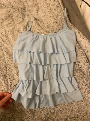 Babyblått linne med volanger  - Söt babyblått linne med volanger i fint skick. Lätt och luftigt, perfekt till sommaren!