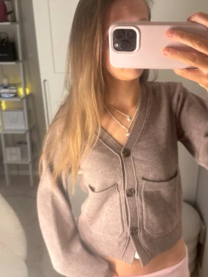 Grå kofta med fickor och knappar - Mysig grå kofta med v-ringning och tre svarta knappar framtill. Koftan har två stora fickor på framsidan och ribbade muddar vid ärmslut och nederkant. Perfekt att slänga på sig över en t-shirt för en chill look.