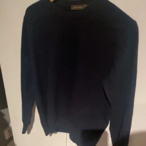 Mörkblå stickad tröja från Oscar Jacobson  - Klassisk mörkblå stickad tröja från Oscar Jacobson med rund halsringning och ribbade muddar vid ärmslut och nederkant. Enkel och stilren design som passar perfekt till skjorta eller t-shirt. Tillverkad i mjukt material för en bekväm känsla.