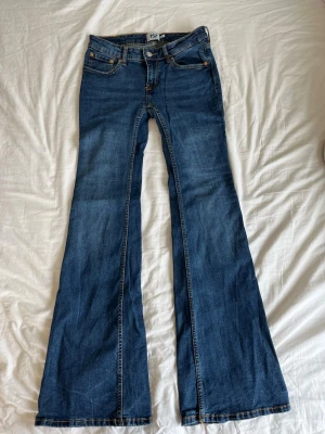 Blå bootcut jeans från 157 - Ett par klassiska blå bootcut jeans från 157 med fem fickor och normal midja. Jeansen har utsvängda ben och är gjorda i mjuk denim med snygga kontrastsömmar. Perfekta för dig som gillar retrovibbar och vill ha en avslappnad men trendig look.