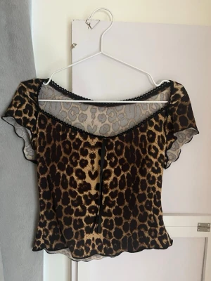 Leopardmönstrad mesh topp - Snygg leopardmönstrad mesh topp med korta ärmar och dekorativ spetskant vid halsen. Toppen har en lätt croppad passform och är tillverkad i ett tunt, transparent material som ger en cool och trendig look.