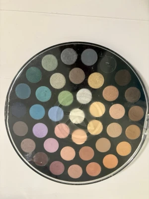 Stor ögonskuggspalett Yves Rocher - Rund ögonskuggspalett från Yves Rocher med 40 olika nyanser. Innehåller både matta och skimrande färger i allt från neutrala beige och bruna toner till färgstarka blå, gröna, lila och rosa nyanser. Perfekt för att skapa kreativa och varierade ögonmakeuper.