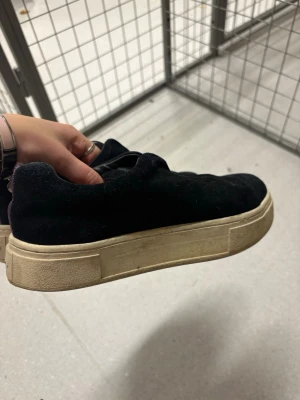 Svarta sneakers från Eytys - Stilrena svarta sneakers från Eytys med tjock vit sula och lila detalj på hälen. Ovandelen är i mockaliknande material och skorna har en klassisk låg profil. Perfekta för dig som gillar en enkel men trendig look.