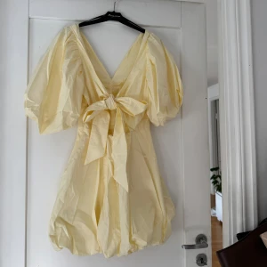 Ljusgul kort puffärmad klänning med rosett - Säljer denna populära klänningen från H&M. den är ljusgul kort klänning med puffärmar och stor rosett i ryggen