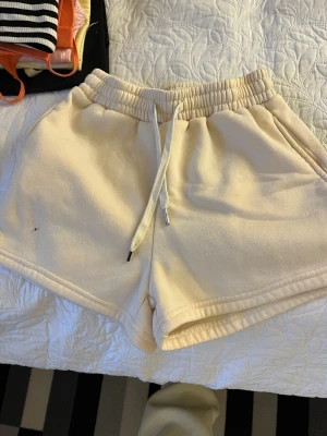 Beige mjukisshorts med snörning - Säljer ett par beige mjukisshorts med elastisk midja och snörning framtill. Shortsen har en avslappnad passform och är perfekta för sommardagar eller chill hemma. Tillverkade i mjukt material för extra komfort.