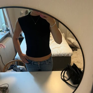 Svart topp från H&M - Svart topp från H&M med ärmlös design. Sitter tight och har snygga rynkade detaljer på sidorna som ger en cool siluett. Materialet är mjukt och stretchigt. Enkel och stilren look som funkar året runt och till fest