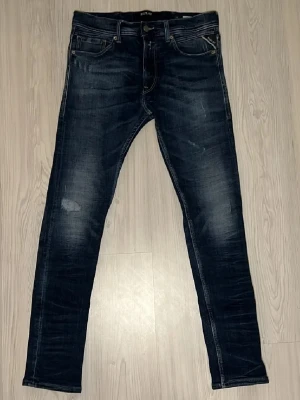 Mörkblå slim fit jeans från Replay - Säljer ett par mörkblå slim fit jeans från Replay med snygga slitningar och klassiska fem fickor. Jeansen har en lätt tvättad look och raka ben. Perfekta för dig som gillar en modern och stilren stil. Storleken är W32, L30. Tveka inte på att höra av dig vid frågor. Priset går att diskutera.