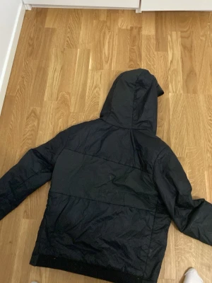 Svart pufferjacka med huva - Säljer en svart pufferjacka från Didriksons med huva och quiltad design. Jackan har en enkel, stilren look och är tillverkad i ett tåligt syntetmaterial som håller värmen under kalla dagar. Perfekt för dig som vill ha en klassisk och funktionell vinterjacka.