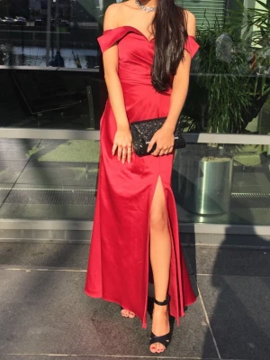 Röd axelbandslös långklänning/balklänning - Elegant röd långklänning med off shoulder-design och hög slits framtill.  Perfekt för bal eller festliga tillfällen. Midja 64 cm, byst 81 cm.