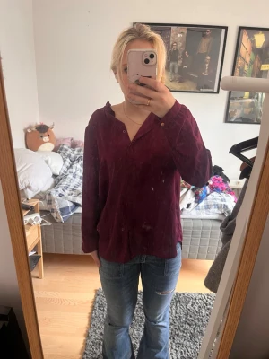 Lila blus med prickar  - Säljer en vinröd blus med avslappnad passform och v-ringning. Blusen har långa ärmar och en knappdetalj vid halsen. Perfekt att styla med jeans för en cool och enkel look.