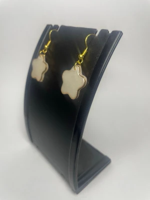 Stjärnformade vita örhängen - Snygga örhängen i form av vita stjärnor med guldfärgade krokar. Stjärnorna har en pärlemorskimrande yta och en tunn guldram runt om. Perfekta för dig som vill ha något gulligt och trendigt till din outfit.