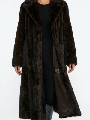 Mörkbrun minkpäls från Saga Mink - Lyxig lång mörkbrun päls från Saga Mink i äkta minkpäls. Kappan har bred krage, rak passform och helfodrad insida med diskret logga. Perfekt för dig som vill ha en statement piece med klassisk vintagekänsla och exklusiv look.