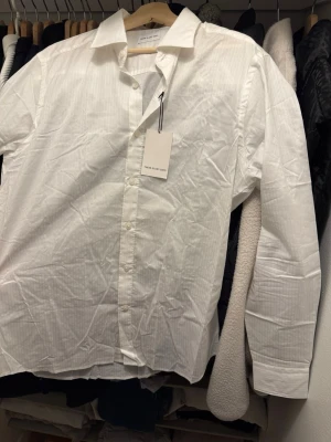 Vit randig skjorta These Glory Days - Klassisk vit skjorta från These Glory Days med diskreta ränder och knappar framtill. Skjortan har lång ärm, krage och är tillverkad i bomull för en skön känsla. Perfekt till både jeans och kostymbyxor.