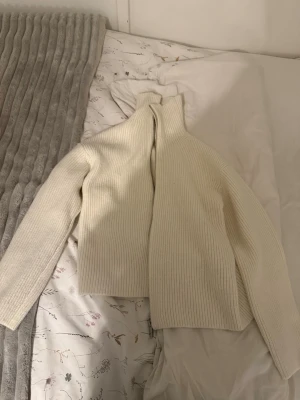 Vit ribbad stickad tröja - Säljer en stilren vit stickad tröja med hög krage och ribbad struktur. Tröjan har långa ärmar och en rak passform som passar perfekt till både jeans och kjol. Enkel men trendig design som är lätt att matcha. Från hm köpt för 600. Aldrig använd.