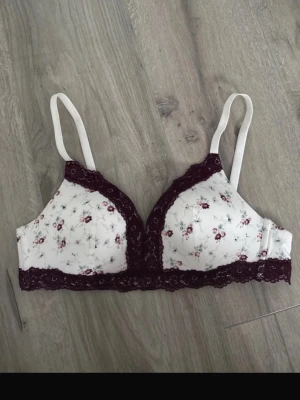 Blommig vit bh med spets - Söt bh med vit bas och små blommor i rosa och grått. Justerbara axelband och klassisk knäppning bak. 