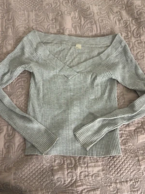 Ljusgrå ribbad v-ringad topp - Snygg ljusgrå ribbad topp med v-ringning och långa ärmar. Toppen har en figurnära passform och är perfekt att styla med jeans eller kjol. Mjuk och stretchig känsla.