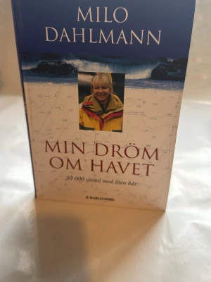 Min dröm om havet av Milo Dahlmann - En inspirerande bok av Milo Dahlmann med titeln 'Min dröm om havet: 30 000 sjömil med liten båt'. Omslaget är blått och vitt med en bild på författaren i gul jacka och havsvågor i bakgrunden. Perfekt för dig som gillar äventyr och havet.