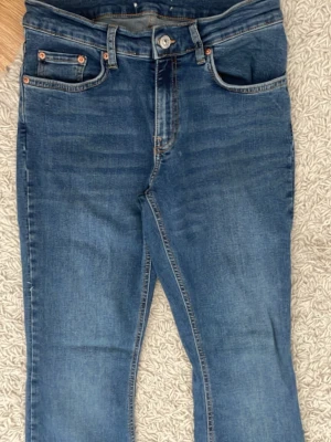 Blå bootcut jeans med utsvängda ben - Säljer ett par klassiska blå bootcut jeans med utsvängda ben och normal midja. Jeansen har fem fickor och är gjorda i ett mjukt denimtyg. Perfekta för dig som gillar retrostil och vill ha ett par jeans som sticker ut lite extra. 