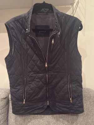 Herno väst  - Snygg svart dunväst från Herno med quiltat mönster och hög krage. Västen har två dragkedjeförsedda fickor framtill och stängs med både dragkedja och tryckknapp vid halsen. Perfekt lager på lager-plagg för kyliga dagar.