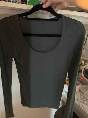 Mörkgrå långärmad topp - En enkel och stilren armégrön långärmad topp med rund ringning. Toppen har en tight passform och är tillverkad i ett mjukt och stretchigt material som känns skönt mot huden. Perfekt att matcha med jeans eller kjol för en clean look