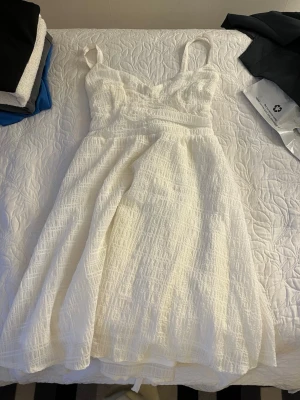 Vit sommarklänning med axelband - Säljer en vit klänning med smala axelband och lätt struktur i tyget. Klänningen har en feminin siluett och är gjord i ett luftigt material som passar perfekt för varma dagar. Stilren och enkel design som är lätt att matcha.