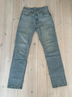 Levi's ljusblå raka jeans - Klassiska ljusblå jeans från Levi's med rak passform och hög midja. Jeansen har fem fickor, gylf med knappstängning och Levi's-lappen bak. Modell 501, storlek W25 L32. Försiktigt använda, säljer pga för små. 
