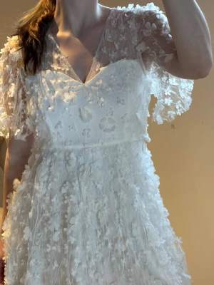 Studentklänning  - Romantisk vit långklänning med v-ringning och transparenta, korta ärmar. Klänningen har ett vackert blommigt spetsmönster över hela plagget och en luftig, flowy passform. Perfekt för speciella tillfällen, exempel stundeten!!  där du vill känna dig extra fin 🤍🌟🩷🎀💕☀️