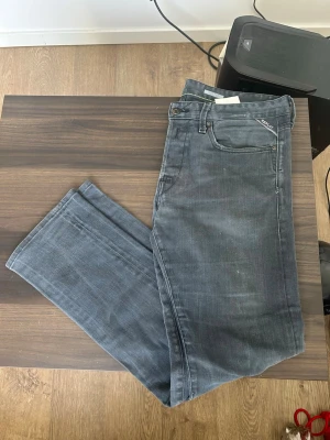 Grå jeans Replay - Säljer ett par grå jeans från Replay med rak passform och klassisk femficksdesign. W33 L32 Jeansen har subtila slitningar och Replay-logga på fickan. Perfekta för en avslappnad och stilren look.