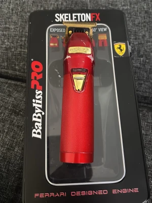 BaBylissPRO SkeletonFX trimmer röd - BaBylissPRO SkeletonFX trimmer i rött med guldfärgade detaljer och exponerat T-blad. Ergonomiskt handtag med greppvänlig yta. Motorn är Ferrari-designad och trimmern passar perfekt för precisa linjer och detaljerad styling. Kommer även med ett nytt blad 