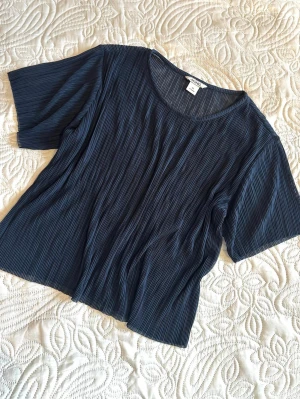 Mörkblå plisserad topp från Monki XS (passar S) - Snygg mörkblå plisserad blus från Monki med korta ärmar och rund halsringning. Tillverkad i ett lätt, transparent material som ger en luftig känsla. Perfekt att styla med jeans eller kjol för en trendig look. Längd ca 50cm, axelbredd ca 38cm.