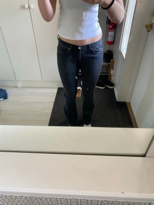 Svarta bootcut jeans med låg midja - Säljer ett par svarta bootcut jeans med låg midja och klassisk femficksdesign. Jeansen har en snygg tvättad look och är perfekta för dig som gillar en avslappnad men trendig stil. Materialet är mjukt och stretchigt för extra komfort.