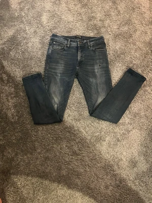 Mörkblå slim fit jeans - Snygga mörkblå slim fit jeans med slitningar och tvättade detaljer. Klassisk femficksmodell med dragkedja och knapp i midjan. Perfekta till en avslappnad streetstyle-look. Materialet är mjukt denim som sitter skönt hela dagen.