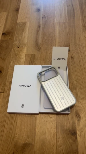 Rimowa iPhone 17 Pro Max skal - Snyggt och exklusivt mobilskal från Rimowa i silverfärgat aluminium med klassiska räfflade linjer. Skalet har en stilren design och är tillverkat i tåligt material som skyddar din mobil. Passar perfekt för dig som gillar minimalistisk och lyxig stil.