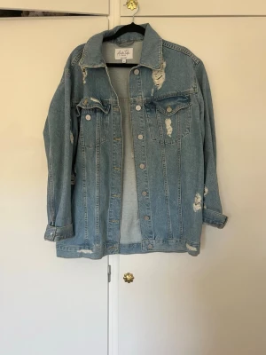 Oversized blå jeansjacka från Angeleye - Snygg oversized jeansjacka i ljusblå denim från Angeleye. Jackan har slitna detaljer, klassisk krage, bröstfickor med lock och knappar framtill. Perfekt för en avslappnad streetstyle-look.
