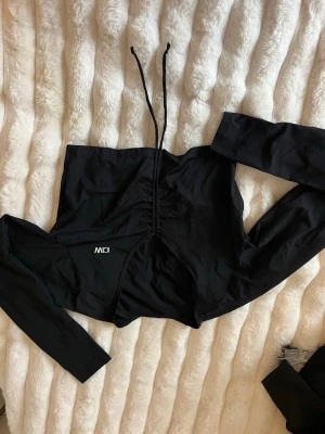 Svart långärmad topp med snörning ICIW - Svart långärmad topp från ICIW med snygg snörningsdetalj framtill och en figurnära passform. Toppen har en modern look med croppad längd och är tillverkad i ett stretchigt material som känns bekvämt mot huden. Passar S och xs 