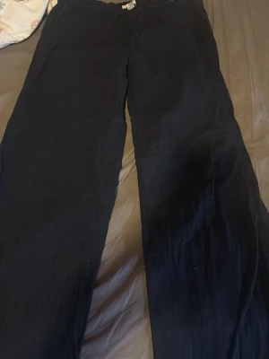 Mörkblå linnebyxor från Gina Tricot - Mörkblå linnebyxor från Gina Tricot med avslappnad passform och resår i midjan. Byxorna har raka ben och är tillverkade i ett lätt och luftigt linnematerial, perfekta för en chill och stilren look.