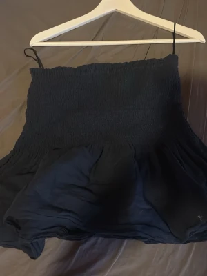 Svart smockad linnetopp Gina Tricot - Svart linnetopp från Gina Tricot med smockad överdel och tunna axelband. Toppen har en flowy, luftig nederdel och är perfekt för varma dagar. Enkel och stilren design som passar till mycket.