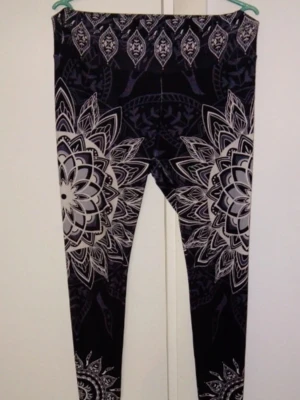 Leggings med mandalamönster - Snygga svarta leggings med stora vita och grå mandalamönster längs benen. Hög midja och stretchigt material som sitter skönt. Perfekta för dig som gillar unika och grafiska prints.