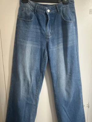Blåa raka jeans med hög midja - Snygga blå jeans med raka ben och hög midja. Jeansen har klassisk femficksdesign och ljus tvätt framtill och baktill för en cool vintagekänsla. Perfekta till sneakers eller boots. 