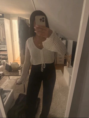 Vit virkad cardigan med knytband - Säljer en vit virkad cardigan med vida ärmar och knytband i midjan. Tröjan har ett luftigt hålmönster och V-ringning, perfekt att slänga över ett linne eller topp. Materialet känns mjukt och lätt, och modellen är croppad. Endast använd 1 gång så i nytt skick.