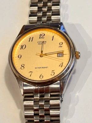 Citizen herrklocka med två armband - Citizen Quartz herrklocka med klassisk rund urtavla i champagnefärg och tydliga svarta siffror. Klockan har datumvisning och levereras med två armband: ett i helsilver och ett i silver/guld. Boetten och armbanden är i metall, perfekt för dig som gillar stilren design.