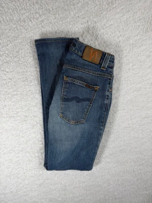Nudie Jeans Tube Tom Light Blue W30/L34 Slim Fit - Tvättad ljusblå denim från Nudie Jeans. Slim fit med stretch för bekväm passform. Modell Tube Tom. Fint använt skick med naturlig fading. Lagade vid skrevet
