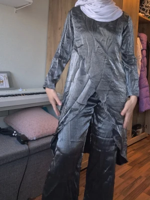 Tröja och byxa set - mörkgrått helt nytt! - Snygg grå långärmad topp i glansigt material  med asymmetrisk nederkant. Toppen har en lös passform och är perfekt för dig som gillar unika detaljer och mjuka material. Byxa följer med resår i midjan!