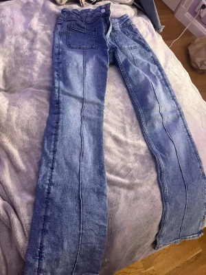 Ljusblå utsvängda jeans med låg midja - Säljer ett par ljusblå jeans med utsvängda ben och låg midja. Jeansen har två bakfickor och synliga sömmar längs benen. Klassisk denimlook som passar till det mesta. Materialet är bomullsdenim.