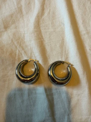 Oanvända silver örhängen från Edblad  - Säljer ett par chunky örhängen i silverfärg med rundad, tjock design. De är klassiska hoops med en modern twist och har en blank finish. Örhängena är från Edblad och är i silver, dem är aldrig heller använda bara ledat i ett smyckeskrin!